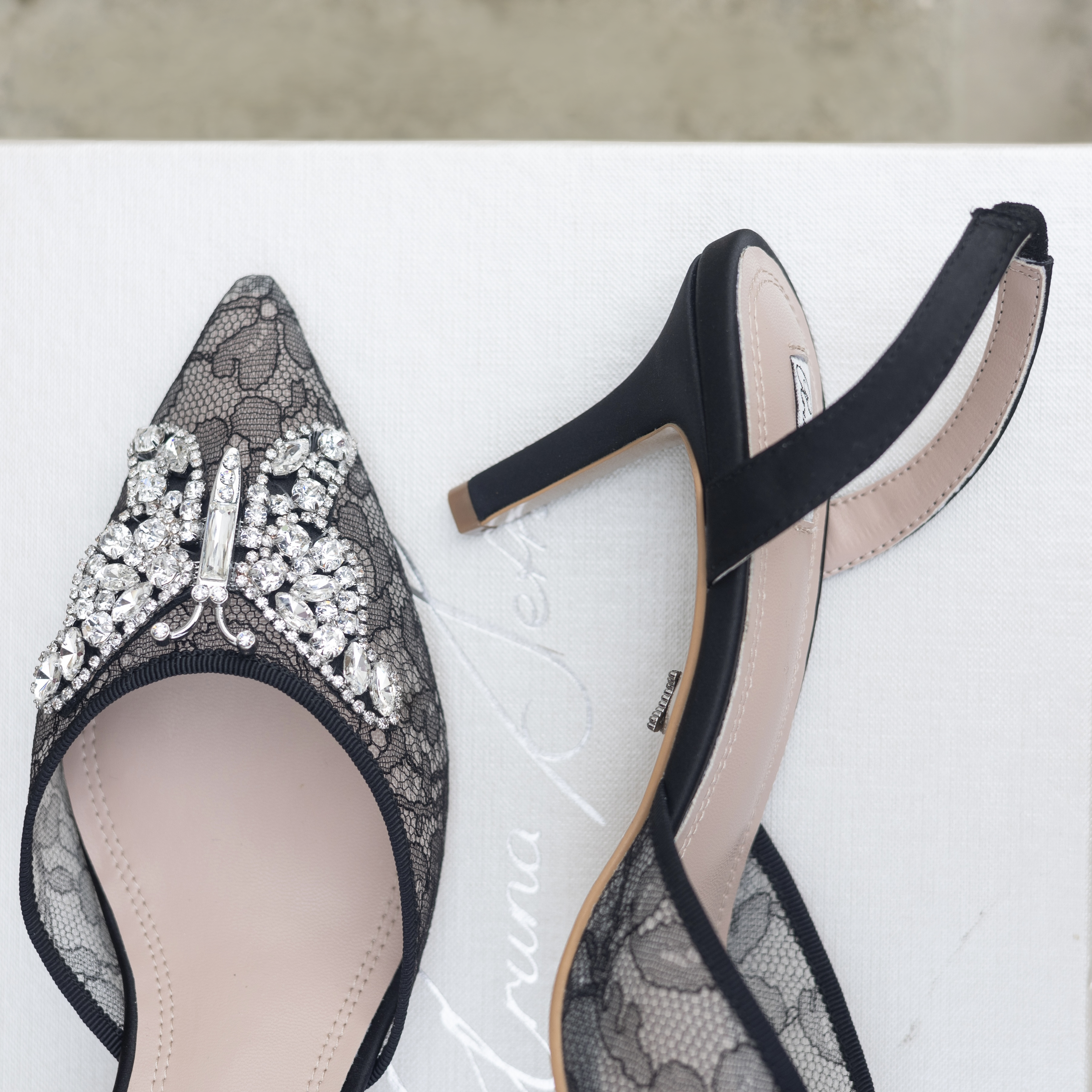 Pair of black lace high heels with embellishments on a white background