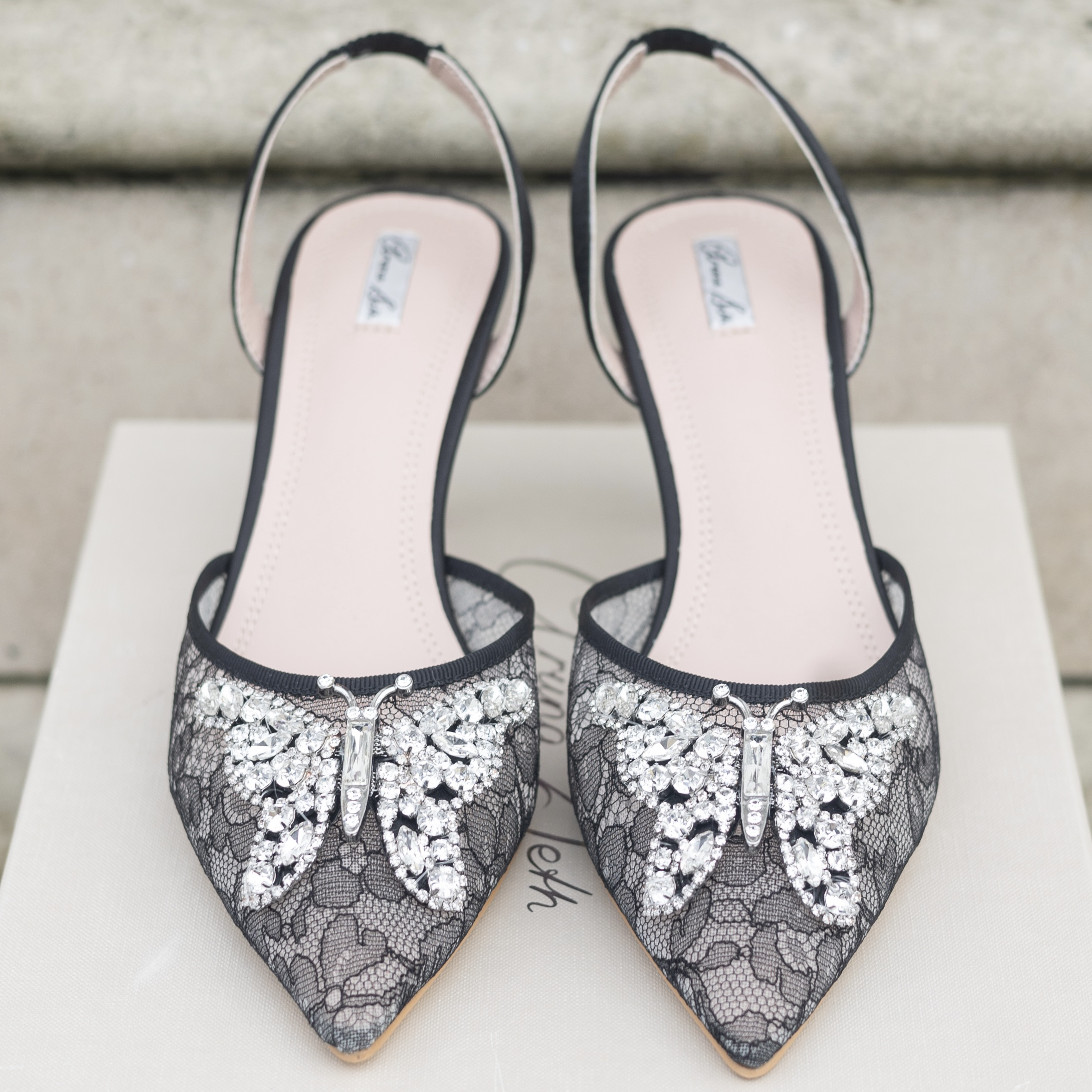 Black lace shoes with butterfly embellishments on a white surface.