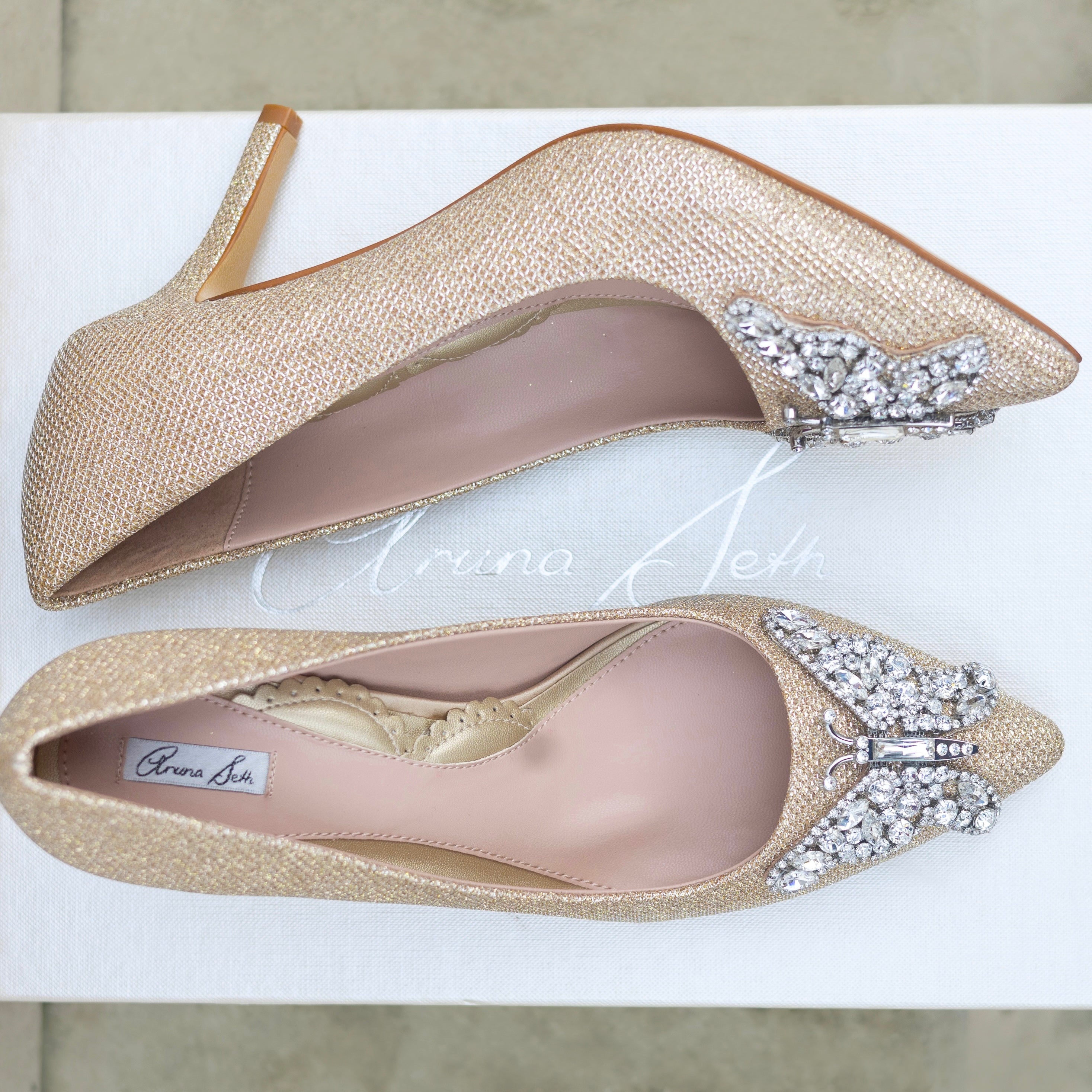 Gold high-heeled shoes with embellishments on a white background